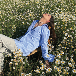 A person in a sun hat relaxing on a green deck chair in a sunny garden with a drink on a nearby table.